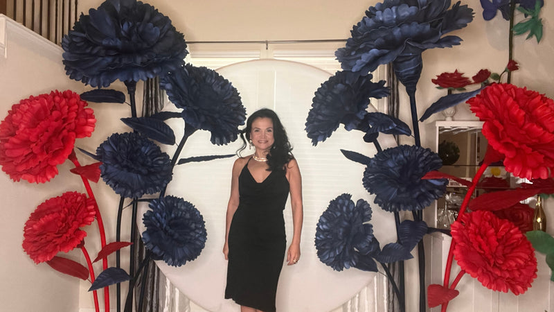 Woman standing in front of a decorative wall with large blue and red flowers.