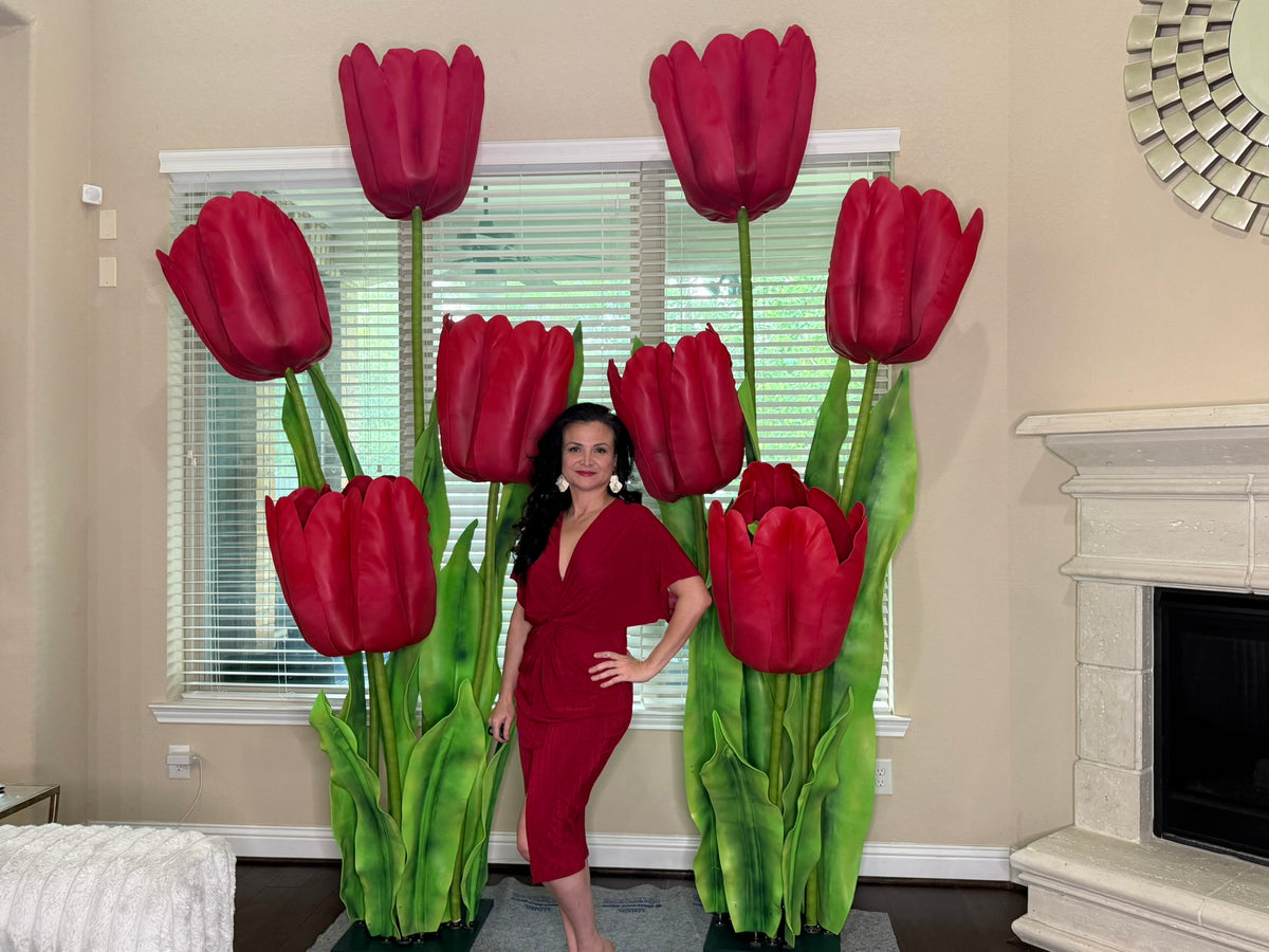 Woman in a red dress standing between two large red tulip sculptures in a living room.